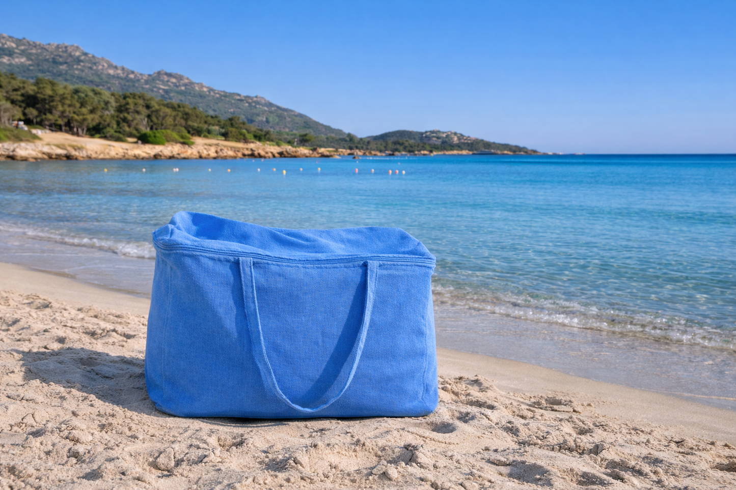 Blue tote bag on a sandy beach with ocean and mountains in the background