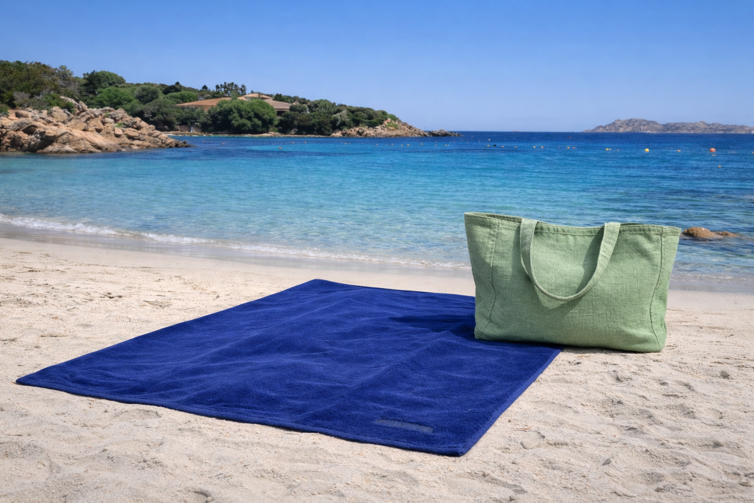 Blue beach mat and green bag on a sandy beach with clear blue water and sky.