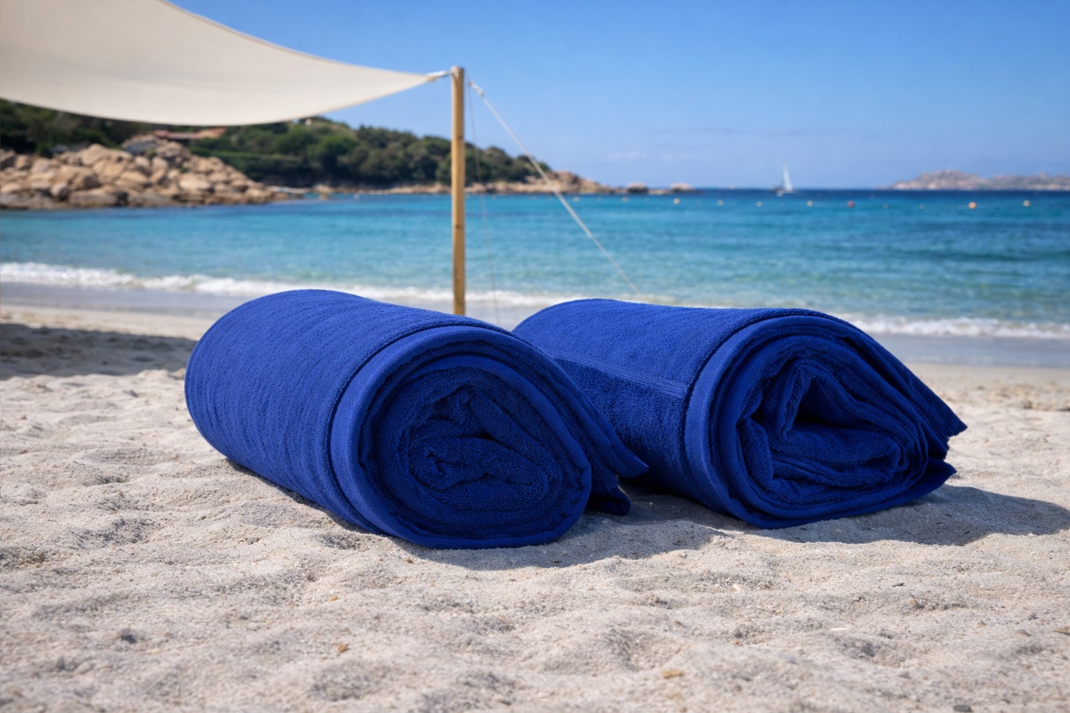 Two blue towels on a sandy beach with ocean and clear sky in the background