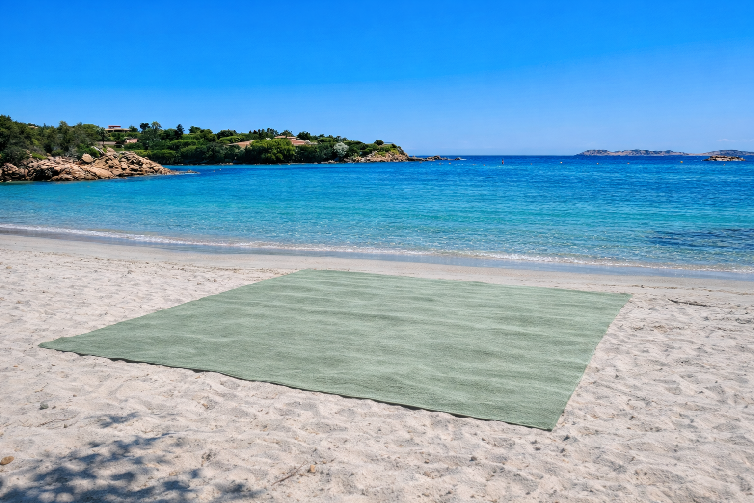 Green beach towel on a sandy beach with clear blue water and sky.
