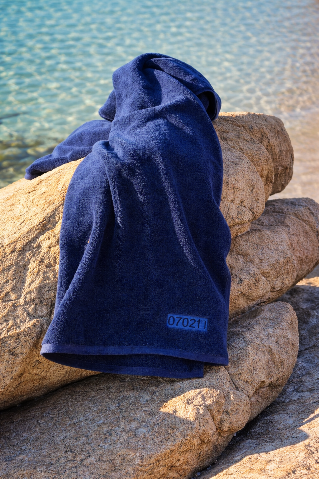 Navy blue towel with a label on a rock by the water