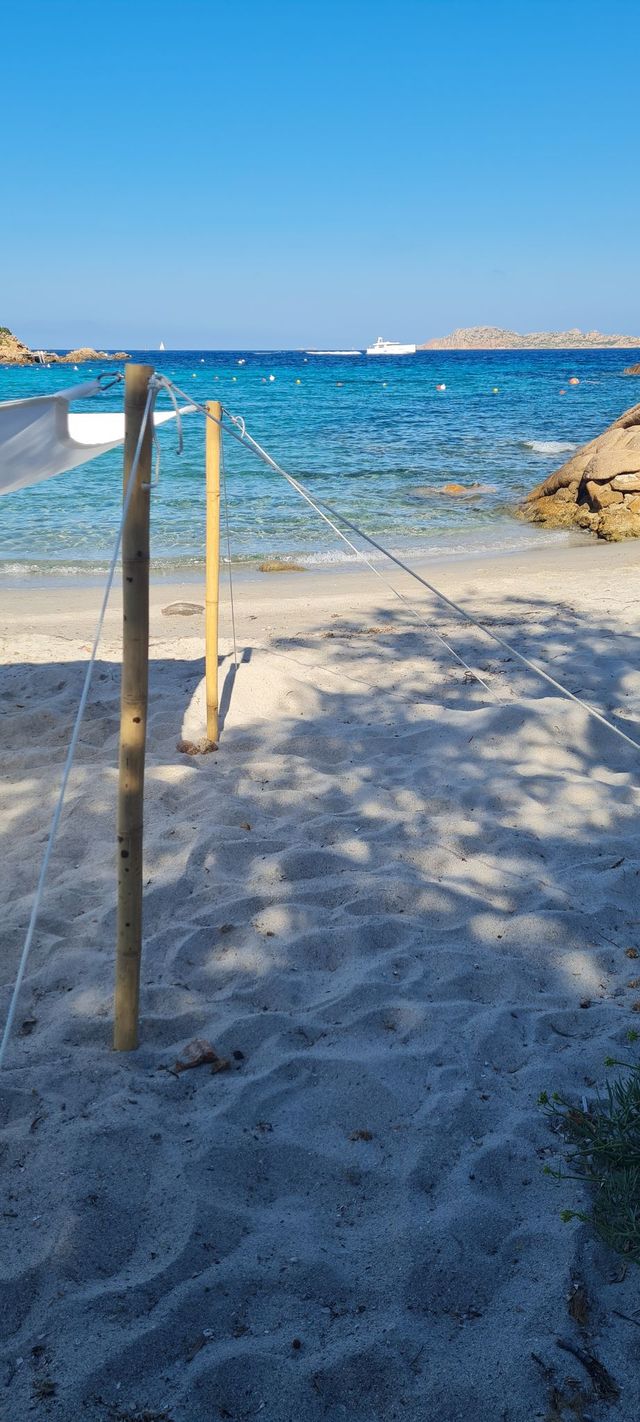 Beach scene with a wooden post and rope, clear blue water, and a boat in the distance.