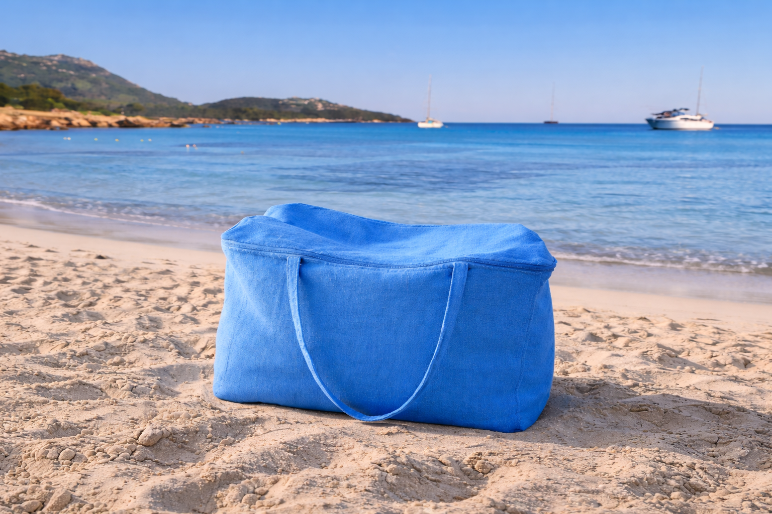 Blue bag on a sandy beach with ocean and boats in the background