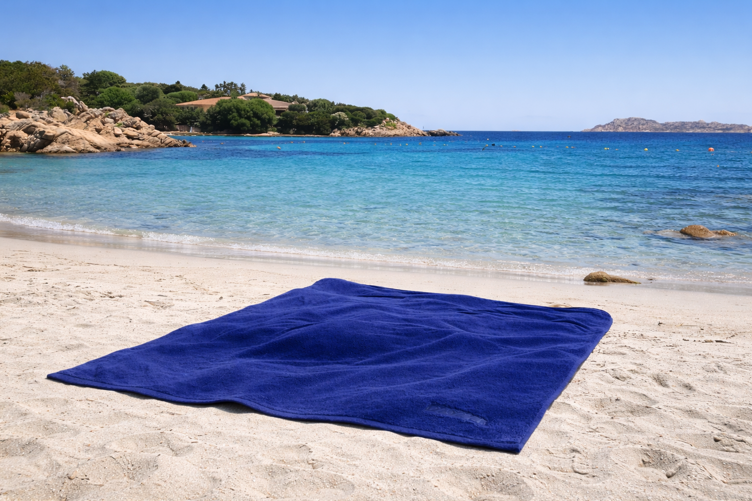 Blue towel on a sandy beach with clear blue water and greenery in the background