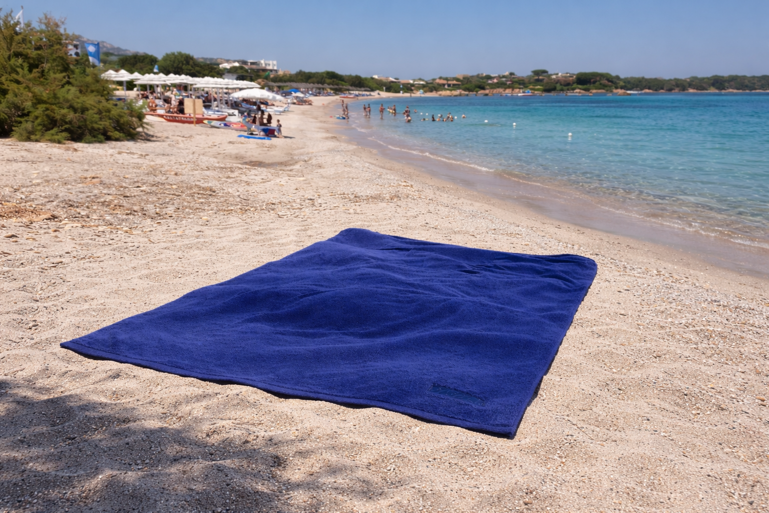 Luxury blue towel on a sandy beach with view over the bay of Romazzino